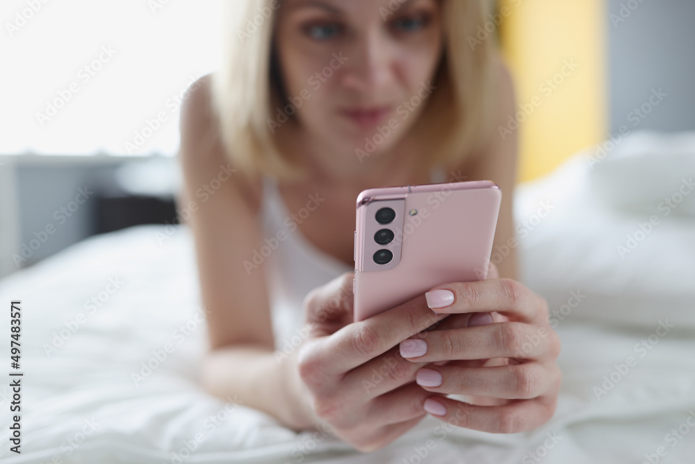 Woman lies in bed and looks at smartphone closeup Woman lies in bed and looks at smartphone closeup