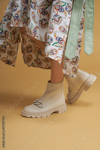 Fashionable woman with beige boots, leather shoes, studio shot. Casual lifestyle concept photo on a yellow pastel background.