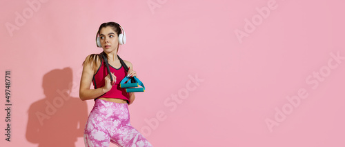Flyer. Professional athlete, young girl training with sports equipment isolated on pink studio background with shadow. Beauty, sport, action, fitness, youth concept.