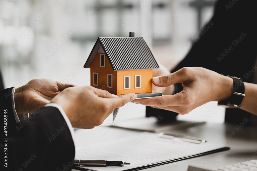 A housing salesman holds a model of a house and sends it to customers as an example, a sample house project where a salesperson advises customers. The concept of selling houses in the project.