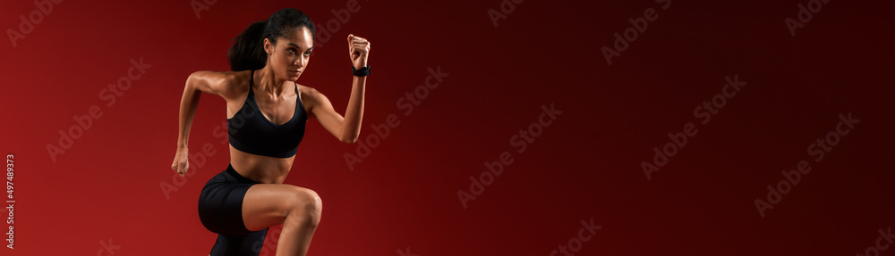 Higher and higher. Full length of young athlete woman in sports clothing jumping against red background Higher and higher. Full length of young athlete woman in sports clothing jumping against red background
