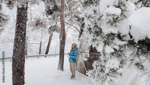 A woman stands and looks at nature with a thermocup in her hands next to a dome tent in glamping in the winter forest photo