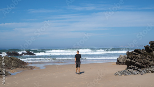 Man on a cold beach. Young man walking to the ocean. Man on a rocky beach with big waves.. Alentejo, Portugal