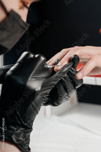 Manicurist with red dreadlocks wearing black gloves doing hardware manicure to male.