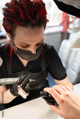 Manicurist with red dreadlocks wearing black gloves doing hardware manicure to male.