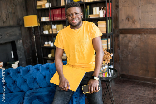 Smiling young african american student or business man professional making business call on the yellow laptop at home enjoying corporate conversation indoors. Joyful freelancer looking in other side