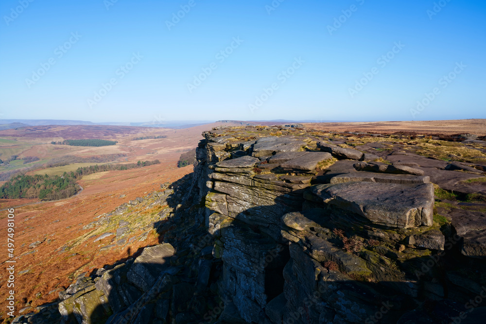 Along the gritstone face of Stanage Edge under a cloudless blue sky.