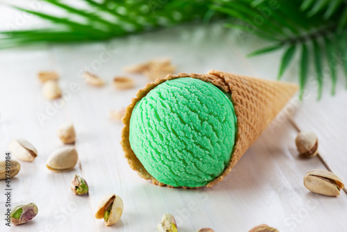 Pistachio ice cream in a cone with a palm branch on a wooden table.