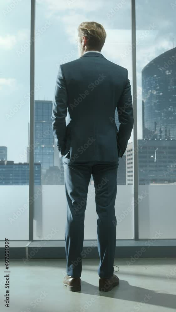Vertical Screen: Successful Young Businessman in a Tailored Suit Standing in Modern Office Looking out of the Window on Big City with Skyscrapers. Successful Finance Manager Planning Project Strategy.