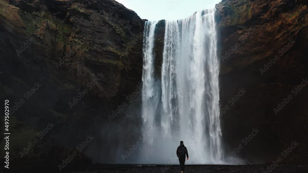 Man walking to Icelandic waterfall Skogafoss in Iceland, near the Skogar, slow-motion background wallpapers. Beautiful landscape. High quality 4k footage. Wide angle shot