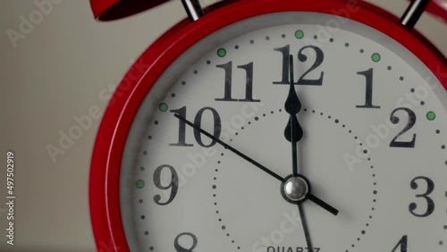 The dial of an old red alarm clock. Twelve o'clock on the clock, the second hand moves from nine to two