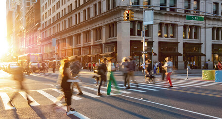 Sunlight shining on people in motion walking across a busy street intersection in Manhattan New York City