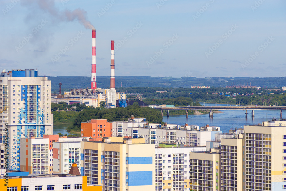 urban landscape - multi-storey residential building and smoking chimneys in an industrial area on the banks of the river