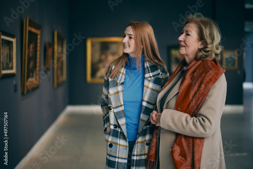 Photo Grandmother and adolescent granddaughter are looking at the paintings in the art gallery