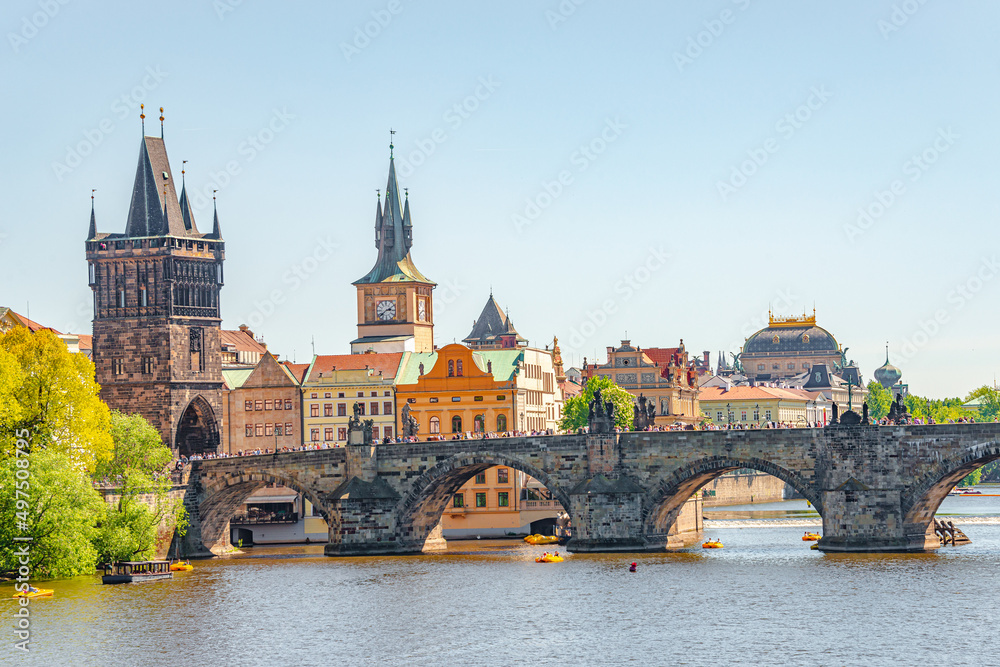 View over magnificent Vltava river with tour boats, tourists and famous Charles Bridge and walking embarkment in historical downtown of Prague, Czech Republic at blue sunset summer sky.