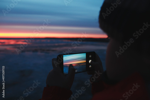 Man hands with mobile cell phone taking a photo of sunset sky at sea. Gradient color. Sky texture. Beautiful abstract nature sunset as background