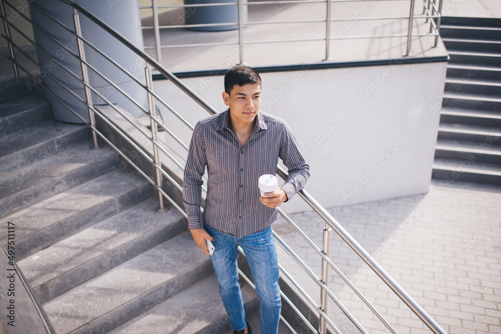 Asian guy with smartphone and coffee on stairs