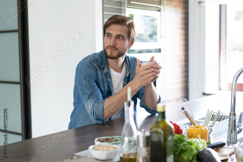 Portrait of man sitting in kitchen holding a cup of coffee looking away in thought