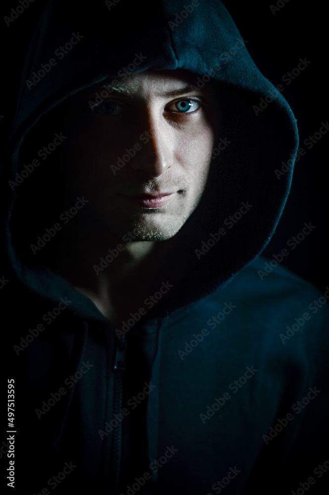 Portrait of a young blue-eyed man with a hood covering his head who in the shadow has a serious and determined look Portrait of a young blue-eyed man with a hood covering his head who in the shadow has a serious and determined look