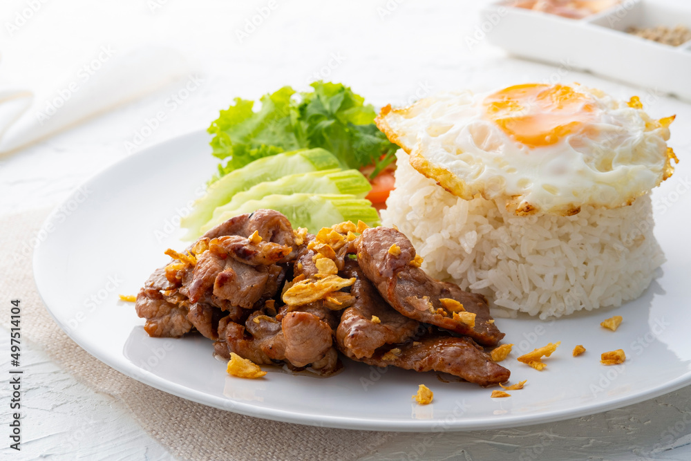 tir-Fried Pork with Garlic and pepper and cooked thai jasmine rice topped with fried egg in white plate,popular Thai food tir-Fried Pork with Garlic and pepper and cooked thai jasmine rice topped with fried egg in white plate,popular Thai food