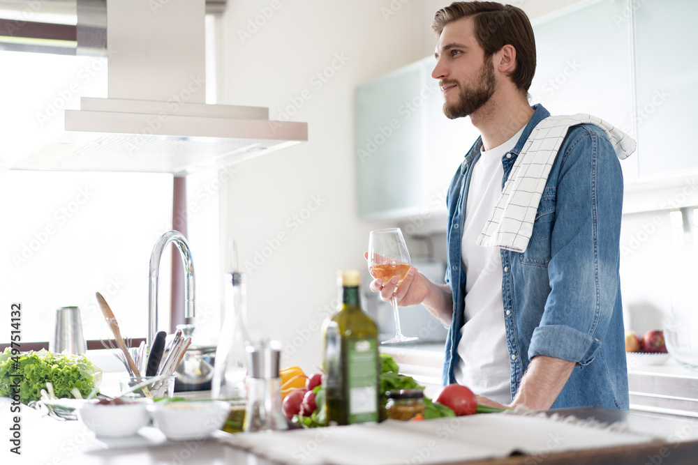 Handsome young man in casual wear drinking wine while standing in the kitchen at home. Handsome young man in casual wear drinking wine while standing in the kitchen at home.
