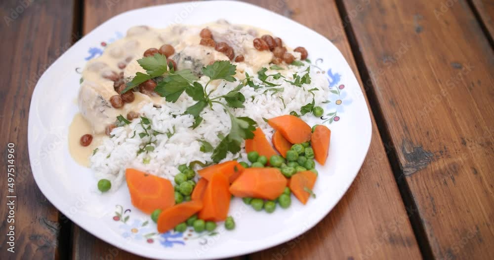 Top view of rice with white sauce and raisins along with boiled meat with carrots and peas on a white plate over the wooden table. cilantro on the top. Top view of rice with white sauce and raisins along with boiled meat with carrots and peas on a white plate over the wooden table. cilantro on the top.