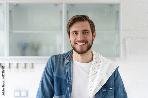 Handsome smiling young man leaning on kitchen counter with vegetables and looking at camera.