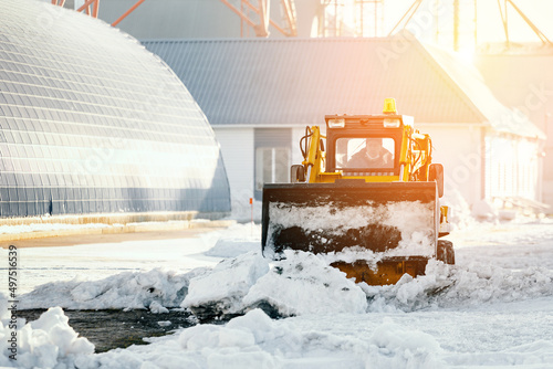 Tractor clears territory of production base from snow on clear winter day. Snow removal after snowfall. Background.