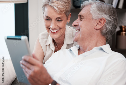 That smile covers my heart. Shot of a mature couple using a digital tablet at home on the sofa together.