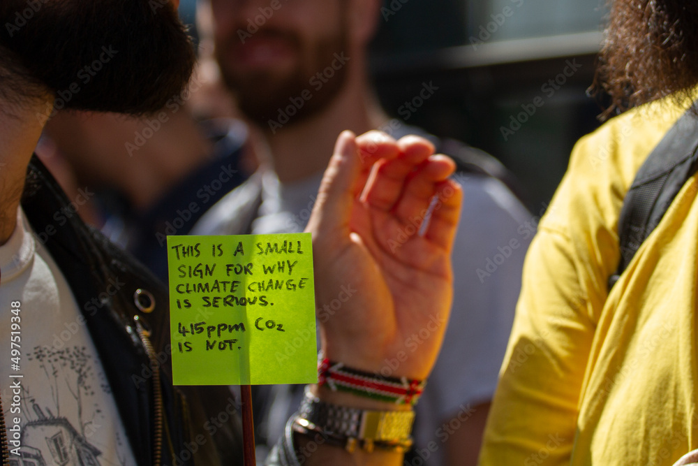 A guy holdning a small and funny sign during a protest for climate change, global warming and environment in Copenhagen, Denmark while discussing - focus on the sign