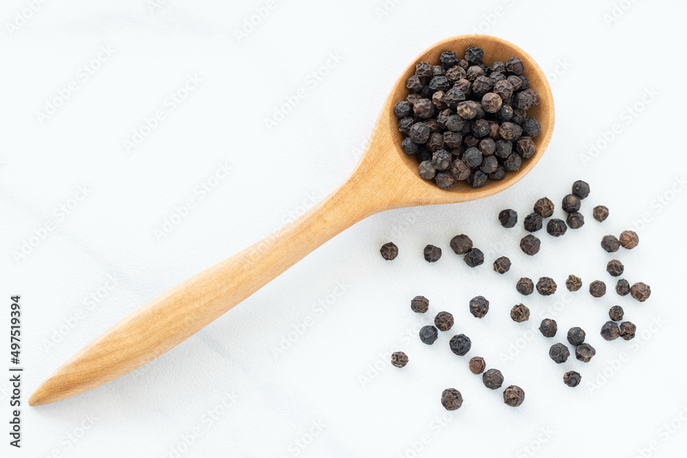 Black peppercorn with a wooden spoon on white background. Composition isolated over the white background. Black peppercorn with a wooden spoon on white background. Composition isolated over the white background.