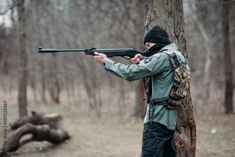 Fototapeta premium Young man aims from pump gun weared in body armor and balaclava.
