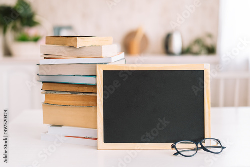 Stack of books with glasses and chalkboard standing on table.