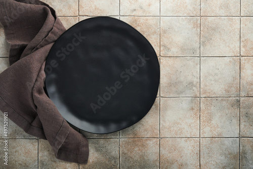 Ceramic empty black plate and linen kitchen towel napkin on old ceramic tile table background. Cooking stone backdrop. Top view with copy space. Flat lay