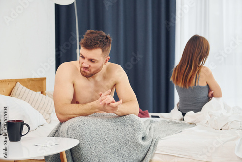 Disappointed woman sitting on the bed with back to the man that feels bad