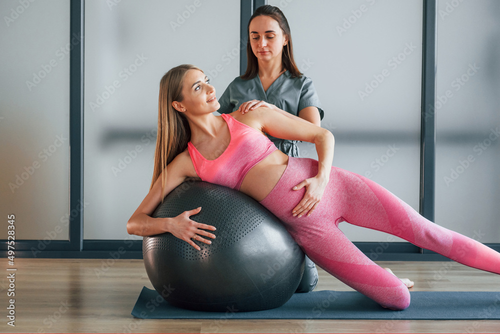 Naklejka premium Using fitness ball. Woman is in health center getting help by doctor