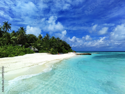 Maldives, the white sand beach with trees near the turquoise ocean. Several people having a rest on a deserted beach.