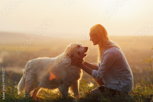 Obraz na płótnie Young woman and golden retriever dog sit on green grass at sunset. Pets friendly travel concept, solar bright light. w salonie