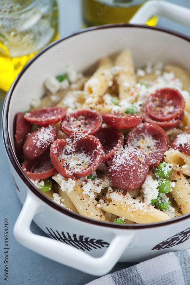 Closeup of a white serving pan with crispy salami, crushed green pea and ricotta pasta, vertical shot