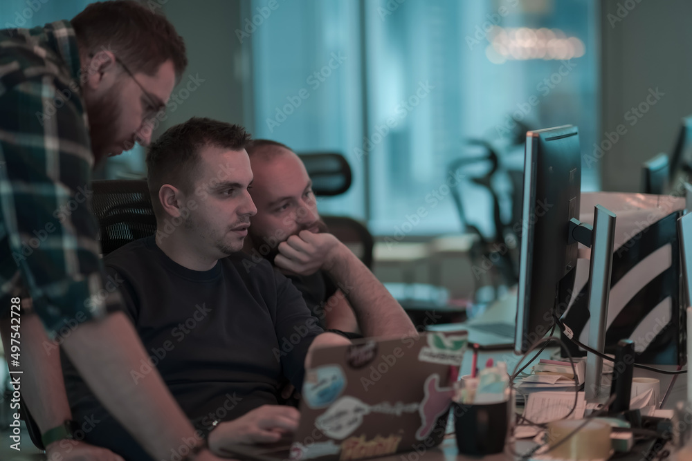 A photo of three men staring intently at a computer while sitting in a modern office. Selective focus A photo of three men staring intently at a computer while sitting in a modern office. Selective focus