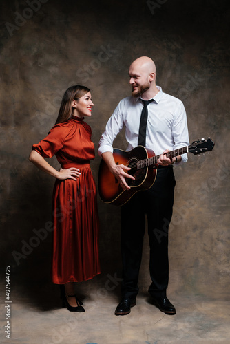A girl in a red dress and musician. Lovely duet posing with guitar. © Евгений Гвоздев
