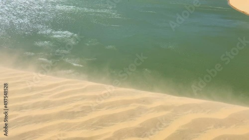 Strong wind moving sand grain at the top of a dune with the lake down there