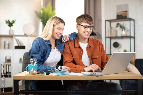 Smiling Caucasian man and woman using modern laptop for work at coworking space or office. Two business partners having working meeting. Concept of cooperation and technology.