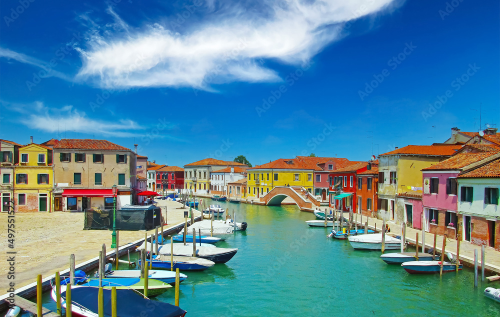 Venice (Murano), Italy - Picturesque calm typical italian town, water canal with boats, bridge, bright colorful houses against clear blue sky, fluffy cloud