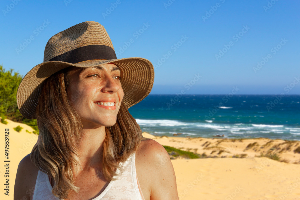 Portrait of young woman with hat smiling on the shore of the beach. Copy space. Selective focus.