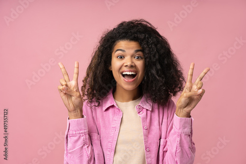 Excited African American woman showing victory sign looking at camera isolated on pink background. Happy female having fun, positive lifestyle 