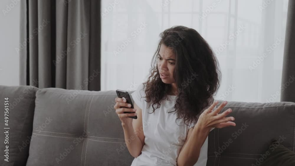 Young African American lady shocked and frustrated looking at phone seeing bad news photos text message with disappoitment and anxiety emotion on face