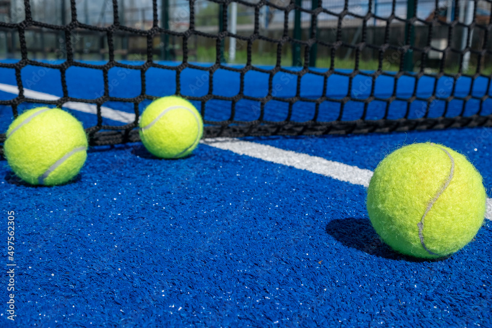three balls near the net in a blue paddle tennis court