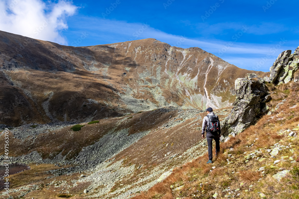 Man with backpack with view on Haemerkogel in the Lower Tauern mountain range, Styria, Austria, Europe. Sunny autumn day in Seckau Alps. Scenic hiking trail to Seckauer Zinken on dry, bare terrain.