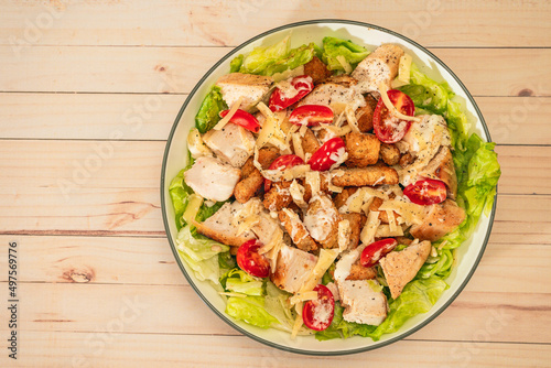 Exquisite variation of Caesar salad with small bites of chicken, cherry tomatoes and a gourmet aioli sauce in a small bowl on a wood table. Top view. small Copy space.